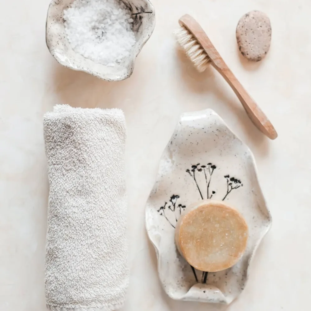 Flatlay met handdoek, borstel en zeep in zachte tinten op een lichte ondergrond